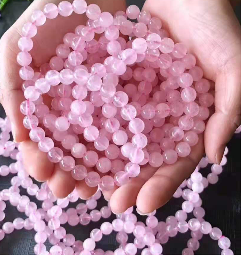 Hands holding multiple genuine rose quartz beaded bracelets with soft pink polished round beads