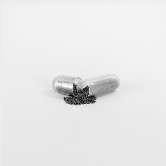 Natural gut wellness supplement capsule with black powder spilled out on white background