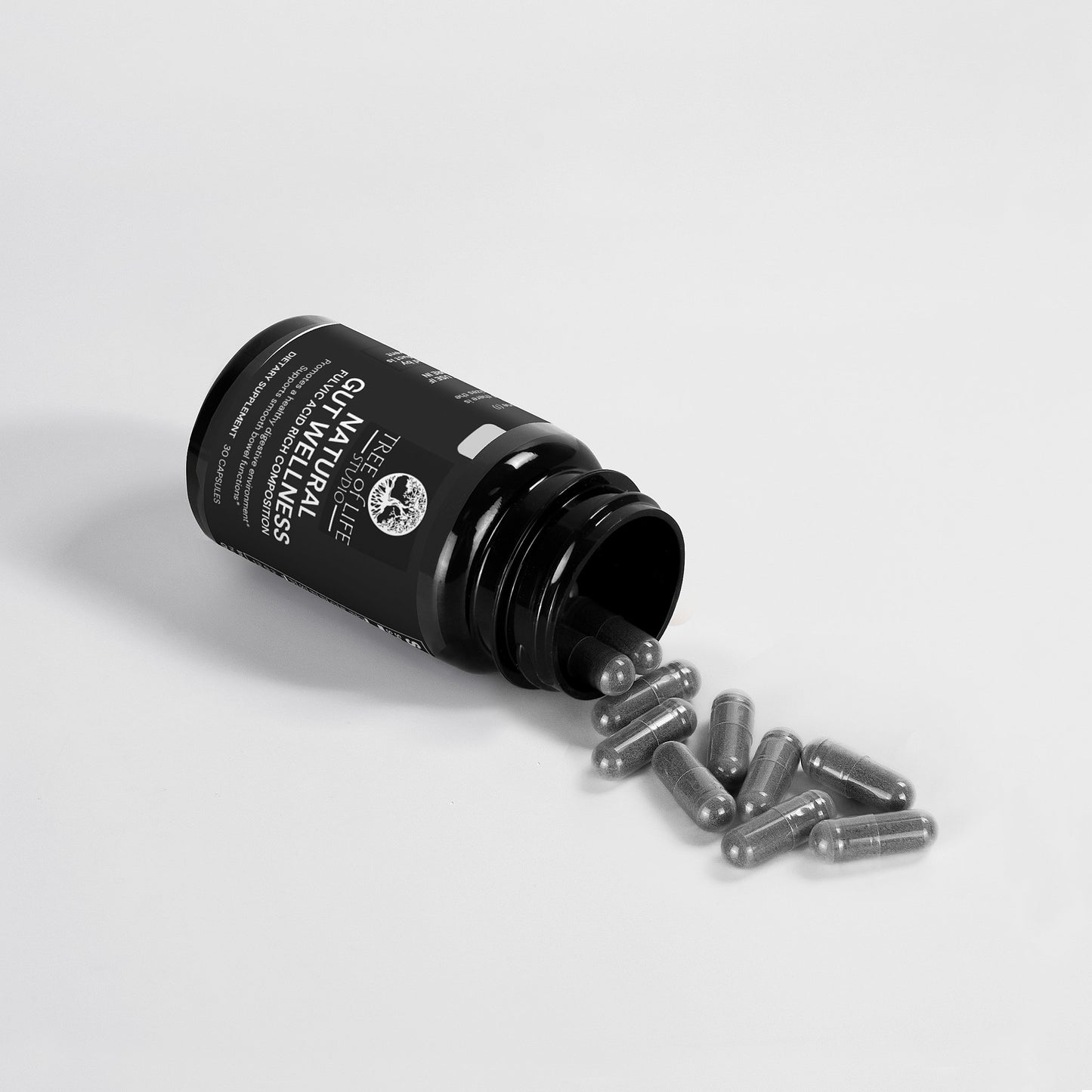 Tree of Life Studio natural gut wellness supplement capsules spilling from black bottle on white background