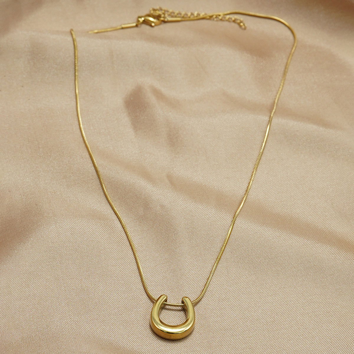Tree of Life Studio 18K gold horseshoe necklace with delicate chain on beige fabric background