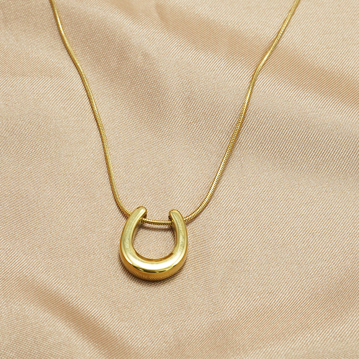 18K gold horseshoe necklace by Tree of Life Studio on beige fabric background