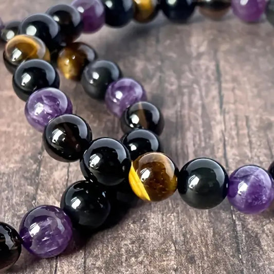 Tree of Life Studio spiritual protection gemstone bracelet with black, purple, and brown beads on wooden background