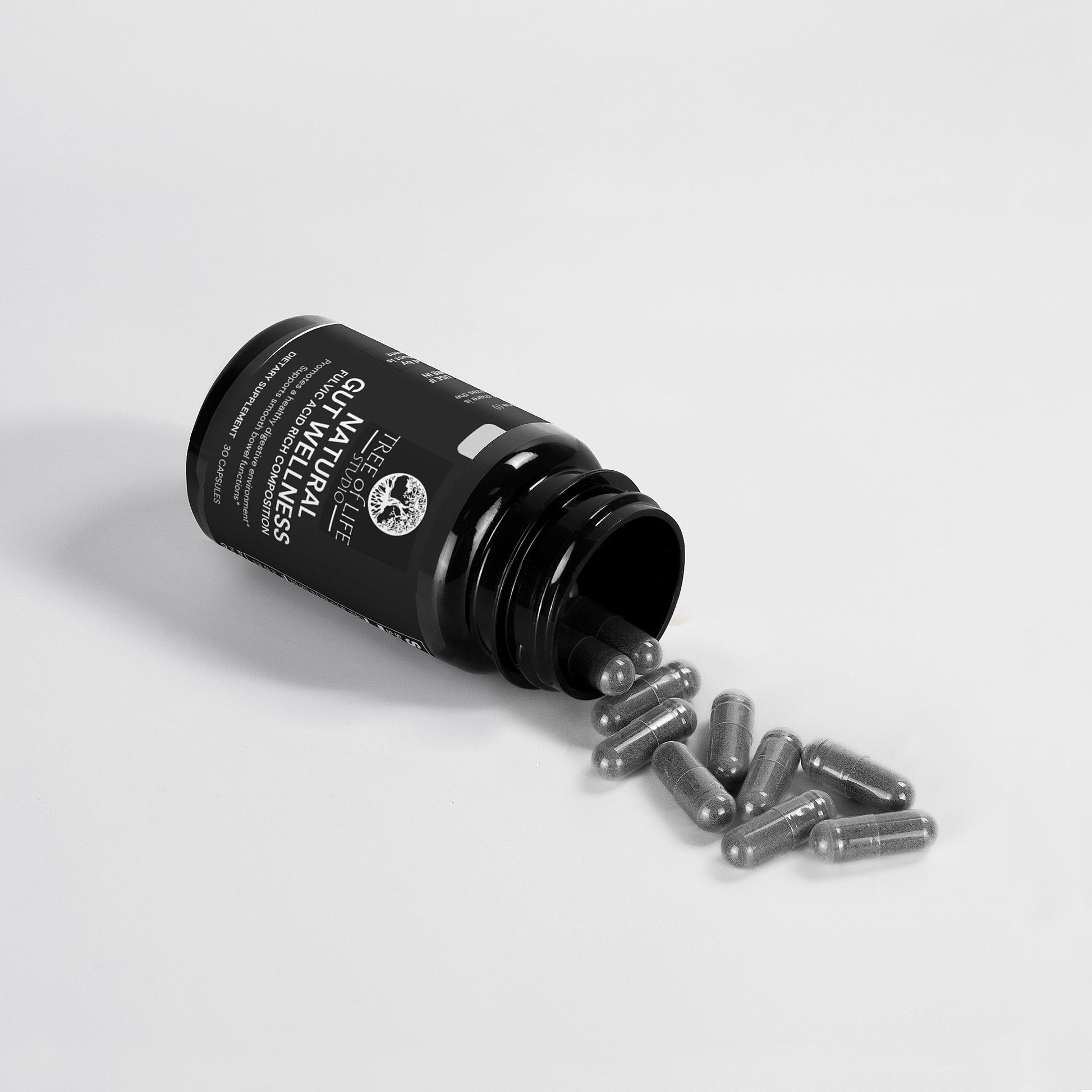 Tree of Life Studio natural gut wellness supplement capsules spilling from black bottle on white background